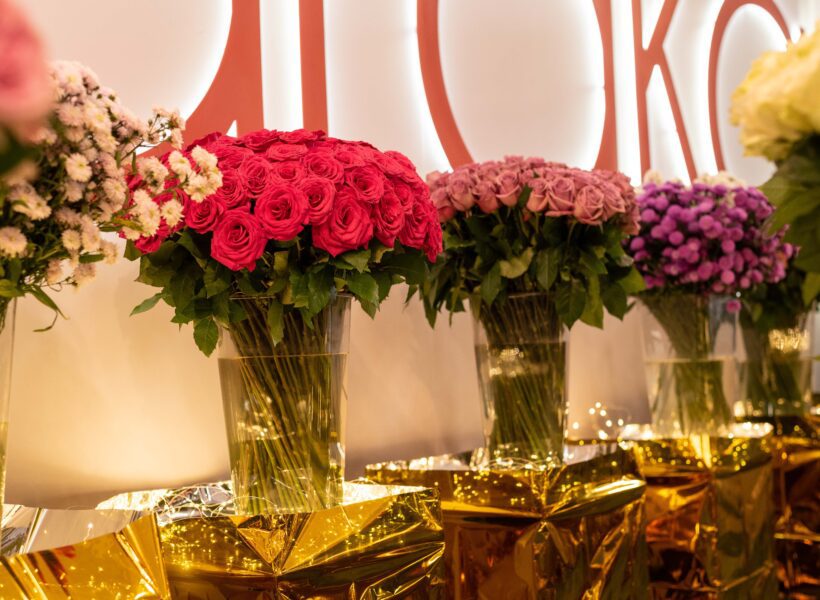 A stunning display of vibrant rose bouquets at the Baraka Roses stand during IFTEX 2024. The arrangement features an array of pink, red, and purple roses, elegantly presented in clear vases with golden wrapping and fairy lights, showcasing the exceptional quality and beauty of Baraka Roses